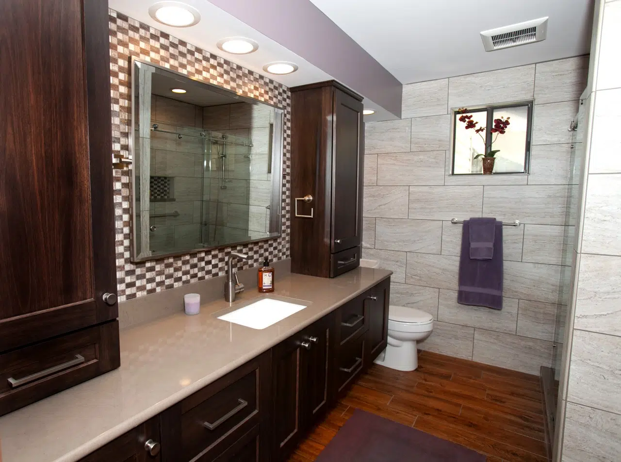 Custom, dark-stained cabinets in a modern door style with contemporary hardware creates a masculine, yet clean-lined look for this large St. Louis bathroom. A colorful mosaic backsplash, large-format porcelain tile walls, and rustic looking floors give the room contrast and character.