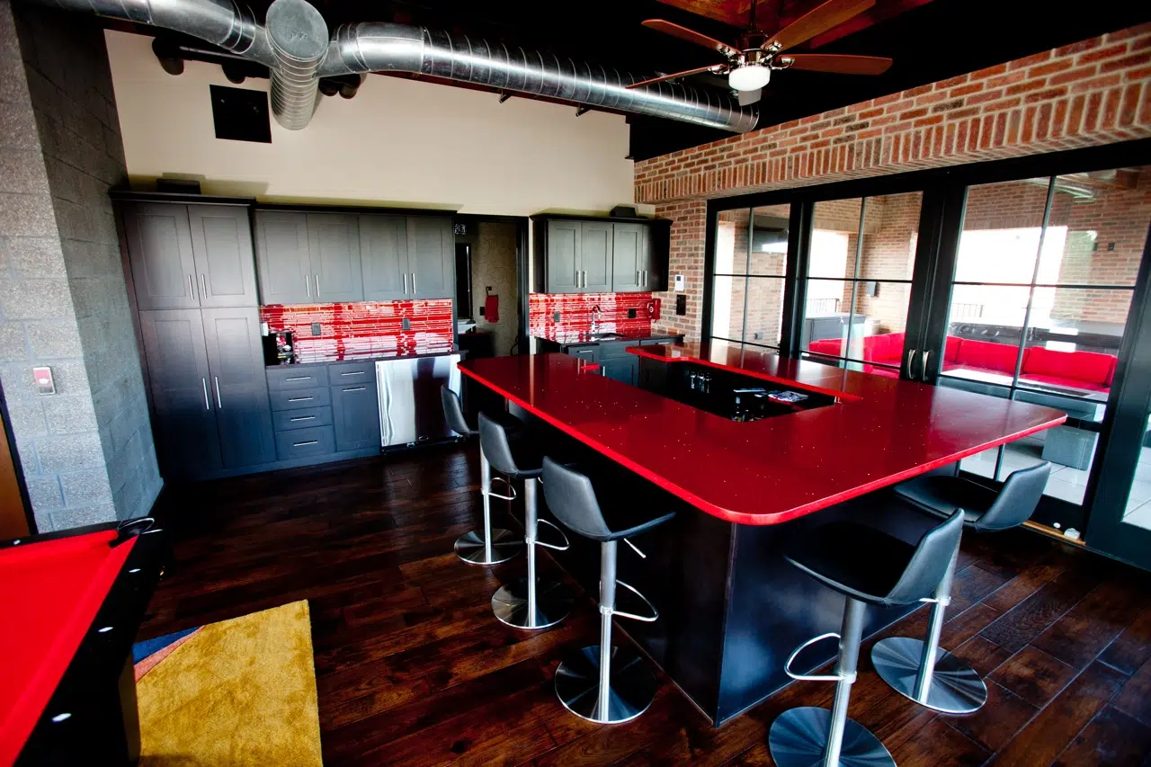 Contemporary bar with red quartz counter and red glass tile back splash in an industrial style new construction home