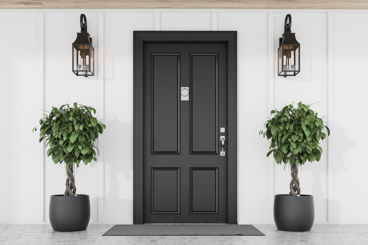 Black front door of white house with trees Stylish black front door of modern house with white walls, door mat, two trees in pots and lamps.